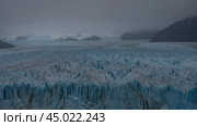 The incredible Perito Moreno Glacier stretches to the horizon between the mountains. An endless mass of blue ice with cracks and sharp peaks. Cloudy. Fog. El Calafate. Argentina. Lago Argentino. (2023 год). Стоковое фото, фотограф Вера Ивановна Кубарева / Фотобанк Лори