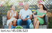 Woman in straw hat is sitting on wooden bench and chatting sweetly with sister and senior father. Стоковое видео, видеограф Яков Филимонов / Фотобанк Лори