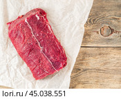 A large piece of raw meat. Beef tenderloin on white parchment paper on rough rustic background, top view, clos up, empty space. Стоковое фото, фотограф Natalia Gdovskaia / Фотобанк Лори