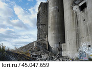 Crumbling concrete silos illustrating urban decay under cloudy sky. Стоковое AI-изображение, AI-художник Иван Рябоконь / Фотобанк Лори