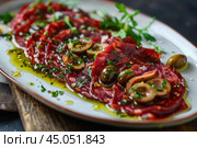 Lomo embuchado appetizer with green olives, herbs and olive oil on a plate. Стоковое AI-изображение, AI-художник Иван Рябоконь / Фотобанк Лори
