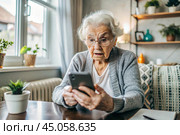 Fraud and deception. A shocked, worried elderly woman looking at her smartphone with unpleasant surprise, experiencing stress, financial problems, money theft. Стоковое AI-изображение, AI-художник Photojuli / Фотобанк Лори