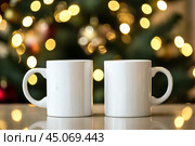 Christmas Mug Mock-Up. Two minimalistic white mugs. Blank white ceramic cups on a desk surface, beautiful warm bokeh lights blurred background. For overlaying your custom quotes, designs for selling. Стоковое AI-изображение, AI-художник Марина Демидюк / Фотобанк Лори