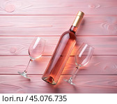 A bottle of rosé wine is laid next to two empty wine glasses on a soft pink wooden surface, creating a light and romantic setting. Стоковое AI-изображение, AI-художник Ольга Игнашина / Фотобанк Лори