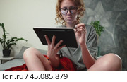 A girl with glasses is surfing the Internet at home in a cozy atmosphere and uses a tablet and a stylus. The glasses reflect the pages you scroll through on the Internet. Стоковое видео, видеограф Енваев Андрей / Фотобанк Лори