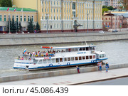 Moscow, Russia, August 2018: Small cruise ship with passengers sails on the Moscow river on a background of  Sofiyskaya embankment (editorial) Редакционное фото, фотограф Михаил Строгалев / Фотобанк Лори
