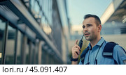 A close-up of a security officer talking on a walkie-talkie, against the backdrop of an urban landscape reflected in the glass facade behind him. Стоковое AI-изображение, AI-художник Ярославский Максим / Фотобанк Лори