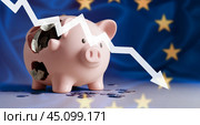 Down arrow and broken piggy bank on Flag of European union. decline in economic indicators in Europe, inflation, stagnation, depression, crisis. arrow falls on background of EU European flag. Стоковое фото, фотограф Павел Муравьев / Фотобанк Лори