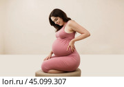 Pregnant woman smiling at her growing belly, cherishing joy of maternity in third trimester. Beautiful pregnant woman hugging her tummy. Стоковое AI-изображение, AI-художник Павел Муравьев / Фотобанк Лори