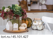 Still-life. A bouquet of decorative cabbage in a vase, pumpkins and white houses on the table in the interior of a home kitchen. A cozy autumn concept. Стоковое фото, фотограф Photojuli / Фотобанк Лори