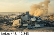 A large pile of discarded electronic waste, including broken computers and monitors, with smoke rising in the background, depicting environmental pollution and the impact of e-waste. Стоковое AI-изображение, AI-художник Башкирова Анна / Фотобанк Лори