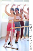 Group of concentrated young female amateur ballet students practicing forward and side battement tendu with arms in third position at barre, improving posture and grace in sunlit mirrored studio. Стоковое видео, видеограф Яков Филимонов / Фотобанк Лори