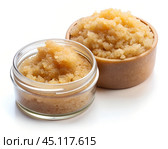 A close-up view of a natural body scrub in a glass jar and wooden bowl, with a grainy texture, set against a white background. Стоковое AI-изображение, AI-художник Ольга Игнашина / Фотобанк Лори