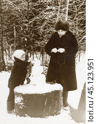 Ребенок и пожилая женщина лепят снеговика на деревянном пне в лесу. 1980-е годы. Стоковое фото, фотограф Retro / Фотобанк Лори