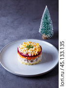 Herring salad under a fur coat. Traditional Russian multilayered salad from herring, beets, potatoes, carrots and eggs. Close-up, selective focus, grey background, miniature Christmas tree. Стоковое фото, фотограф Наталья Любина / Фотобанк Лори