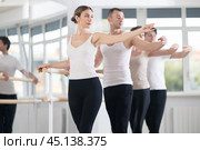 Pretty young girl in black and white sportswear, participating 2nd position of ballet stance at barre with group in choreography studio. Стоковое фото, фотограф Яков Филимонов / Фотобанк Лори