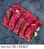 Raw meat, beef steak with seasoning on black stone table, top view. Стоковое фото, фотограф Natalia Gdovskaia / Фотобанк Лори