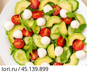 Fresh salad - tomatoes, cucumbers, arugula, mozzarella, avocado. Oil with spices, rosemary thyme, top view, close up. Стоковое фото, фотограф Natalia Gdovskaia / Фотобанк Лори