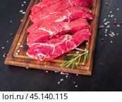Raw meat, beef steak with seasoning on chopping board on dark background with rosemary, Стоковое фото, фотограф Natalia Gdovskaia / Фотобанк Лори