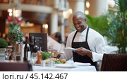 A happy waiter serving gourmet cuisine in an elegant restaurant filled with delighted diners during dinner time. Стоковое AI-изображение, AI-художник Сергей Толмачёв / Фотобанк Лори