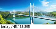 Modern cable-stayed bridge spanning a river on a sunny day. Стоковое AI-изображение, AI-художник Юрий Поздников / Фотобанк Лори