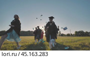 College graduates run into the sunset and throw books and notebooks up in the air. Стоковое видео, видеограф Mikhail Davidovich / Фотобанк Лори