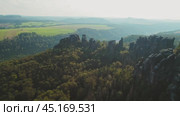 Rugged rock formations covered with trees, extending over green fields and distant hills. Schrammsteine in the Elbe Sandstone Mountains Germany. (2024 год). Стоковое видео, видеограф Igor Tichonow / Фотобанк Лори
