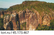 A towering sandstone rock formation rises above a forested area, illuminated by the soft light of the setting sun, showing weathered rock textures. Стоковое видео, видеограф Igor Tichonow / Фотобанк Лори