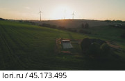 Sunset casts a warm glow on wind turbines in the distance over a patchwork of green agricultural fields. Стоковое видео, видеограф Igor Tichonow / Фотобанк Лори