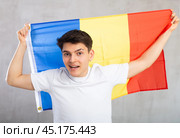Happy young man holding flag of Romania against unicoloured background. Стоковое фото, фотограф Яков Филимонов / Фотобанк Лори