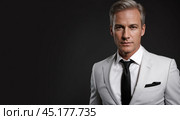 Successful businessman with crossed arms in magnificent white suit stands on dark background. portrait of charismatic billionaire. Стоковое AI-изображение, AI-художник Павел Муравьев / Фотобанк Лори