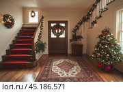 A festively decorated hallway with a staircase leading to the second floor. Garlands of fir branches decorated with lights are hung on the walls and railings, giving the room a warm atmosphere. A Christmas wreath with a red ribbon hangs on the door, emphasizing the festive mood. In the corner there is a decorated Christmas tree with red and gold balls, decorated with ribbons and garlands. On the floor there is a rug with an oriental pattern, adding coziness and warmth to the room. Стоковое AI-изображение, AI-художник Анна Кривицкая / Фотобанк Лори