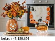 A vase of flowers,a jack pumpkin and candles on a tray. In the background - the interior of a white kitchen in Scandi style. The concept of home and comfort. Autumn decor for the Halloween holiday. Стоковое фото, фотограф Photojuli / Фотобанк Лори