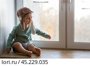 A cute 2-year-old boy in a cap is playing on the windowsill with a wooden airplane. Children's wooden toys for child development. Стоковое фото, фотограф Photojuli / Фотобанк Лори