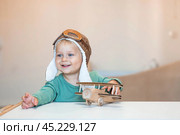 A handsome little boy of 2 years old in a pilot's hat is playing with a wooden airplane and a logistics constructor. Children's wooden toys for child development. Стоковое фото, фотограф Photojuli / Фотобанк Лори