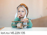 A handsome little boy of 2 years old in a pilot's hat is playing with a wooden airplane and a logistics constructor. Children's wooden toys for child development. Стоковое фото, фотограф Photojuli / Фотобанк Лори
