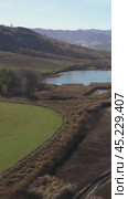 Vertical drone video of flying over a hilly rural landscape with a winding road and fish ponds. Altai Krai. Стоковое видео, видеограф Сергей Пристяжнюк (Serg Zastavkin) / Фотобанк Лори