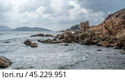 Coastal waves crash against monumental granite boulders lining shore. majestic seascape features vast expanse of rocks, under turbulent, cloud-laden sky, untamed natural panorama. Стоковое фото, фотограф Павел Муравьев / Фотобанк Лори