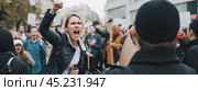 Woman passionately yelling during protest, surrounded by crowd of demonstrators on city streets, expressing strong emotions. Стоковое AI-изображение, AI-художник Павел Муравьев / Фотобанк Лори
