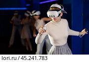 Emotional girls in VR headsets fully immersed in game, engaged in virtual reality world, manipulating objects or shooting targets with joysticks in hands. Стоковое фото, фотограф Яков Филимонов / Фотобанк Лори