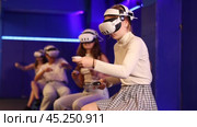 Four cheerful emotional young female friends in VR goggles sitting in virtual reality room, manipulating objects or shooting at targets with gaming controllers in hands. Стоковое видео, видеограф Яков Филимонов / Фотобанк Лори