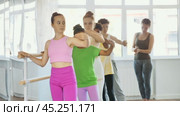 Group of concentrated teenage students of ballet school diligently practicing Demi rond de jambe par terre at barre in sunlit mirrored choreographic studio to applause of smiling female choreographer. Стоковое видео, видеограф Яков Филимонов / Фотобанк Лори