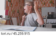 The boy solves math, does homework in the kitchen and yawns from boring tasks. The child writes the answer to the solution of the example in a notebook. The kid sits at the table and performs the task. Стоковое видео, видеограф Екатерина Золина / Фотобанк Лори