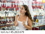 Female buyer holds in hands tests edged weapons in memorable gifts shop. Стоковое фото, фотограф Яков Филимонов / Фотобанк Лори