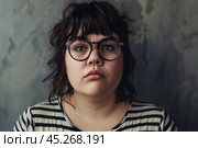 Ugly Young plus size woman wearing casual clothes and glasses sad expression on face with grey background. Apathy, depression, bulling, harassments concept. Social problem of fat people. Стоковое AI-изображение, AI-художник Sergey Grishin / Фотобанк Лори