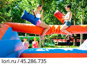 Laughing young girl fighting by pillows with female opponent on inflatable beam. Стоковое фото, фотограф Яков Филимонов / Фотобанк Лори