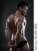 Handsome muscular bodybuilder posing on gray background. Low key studio shot. Стоковое фото, фотограф Станислав Тарко / Фотобанк Лори