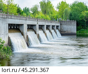 Dam with Waterfall on the River. Hydroelectric dam during Spring runoff, full water. Water rushing out of opened gates of hydro electric power dam. Concrete foothill and wall. Renewable energy systems. Стоковое AI-изображение, AI-художник Марина Демидюк / Фотобанк Лори