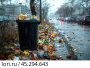An overflowing trash bin on a city street on a rainy day. Waste, including plastic bottles, bags and other trash, is scattered around the bin, creating an atmosphere of pollution and disrepair. Cars and tree silhouettes can be seen in the distance, heightening the contrast between urbanization and lack of cleanliness. The gray sky and wet asphalt emphasize the gloominess of the scene, symbolizing environmental problems and the need to care for the environment. Стоковое AI-изображение, AI-художник Анна Кривицкая / Фотобанк Лори