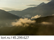 Soft mist blankets the mountains during sunrise, creating a tranquil atmosphere in a secluded valley. Cloud formations drift lazily as the sun rises. Стоковое фото, фотограф Алексей Климкин / Фотобанк Лори